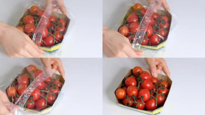 女人用食物薄膜在白色桌子上储存食物。一次性塑料包装的樱桃番茄。慢动作视频。特写