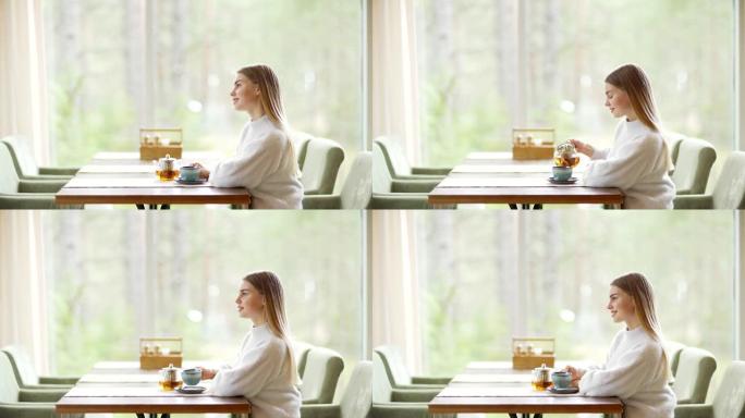 侧视图缩小镜头，美丽的年轻女子独自坐在咖啡桌，喝着茶，幻想着她的脸上的微笑