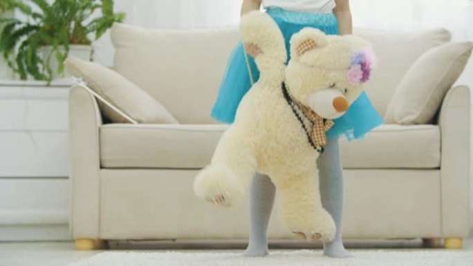 穿着蓝色裙子的小女孩的短腿站着，戴着一条长毛绒的泰迪熊，戴着项链和有趣的头饰。