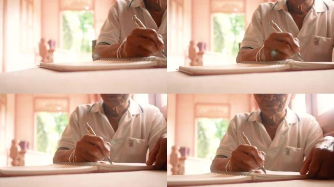 高年级男子在一张纸上写下信件。关闭老男性的手在笔记本上写下当天的备忘录。