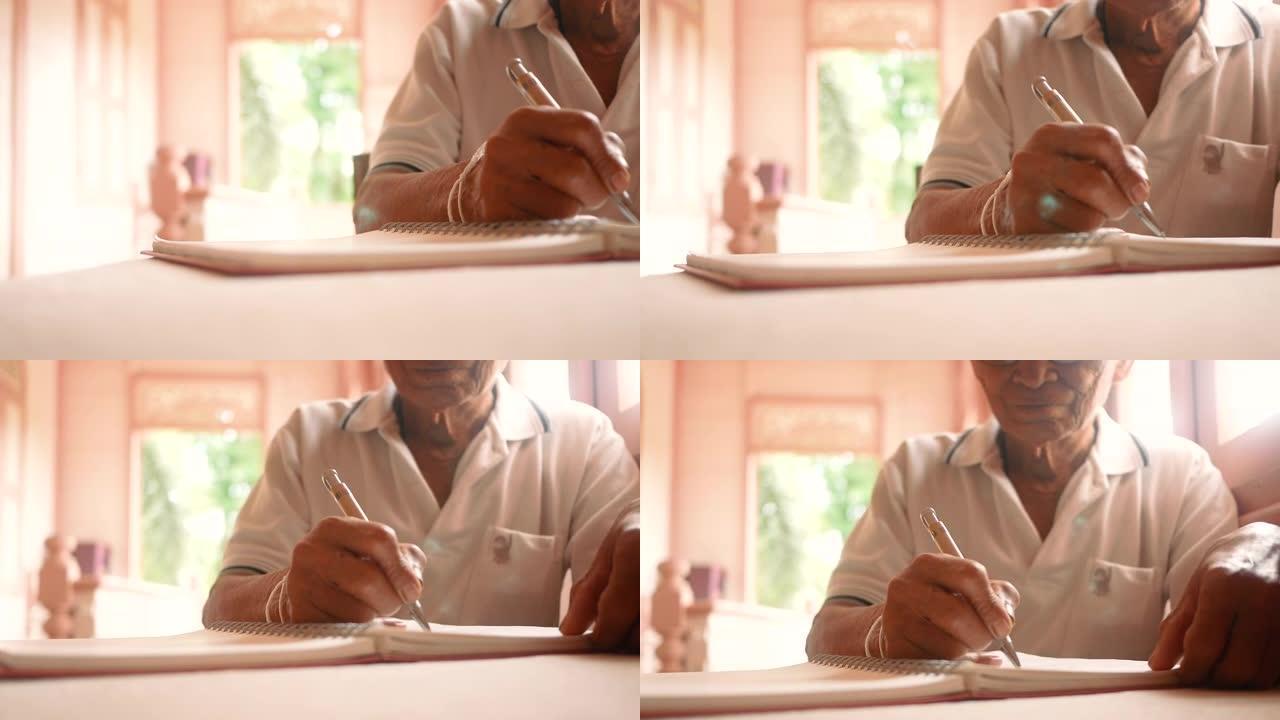 高年级男子在一张纸上写下信件。关闭老男性的手在笔记本上写下当天的备忘录。