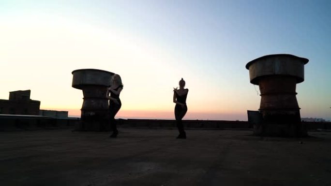日落时在工业屋顶上跳舞的优雅女孩的剪影