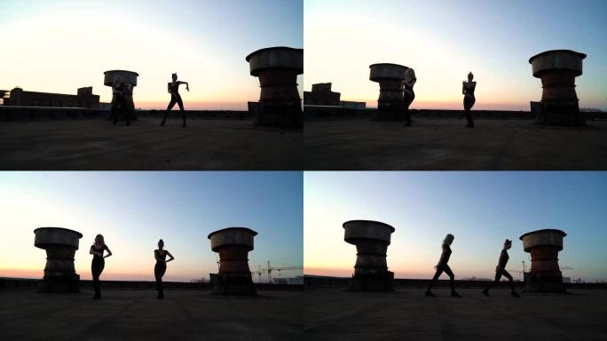日落时在工业屋顶上跳舞的优雅女孩的剪影