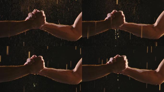 两个肌肉发达的男人在雨滴和许多飞溅的黑色背景上握手。慢动作。特写