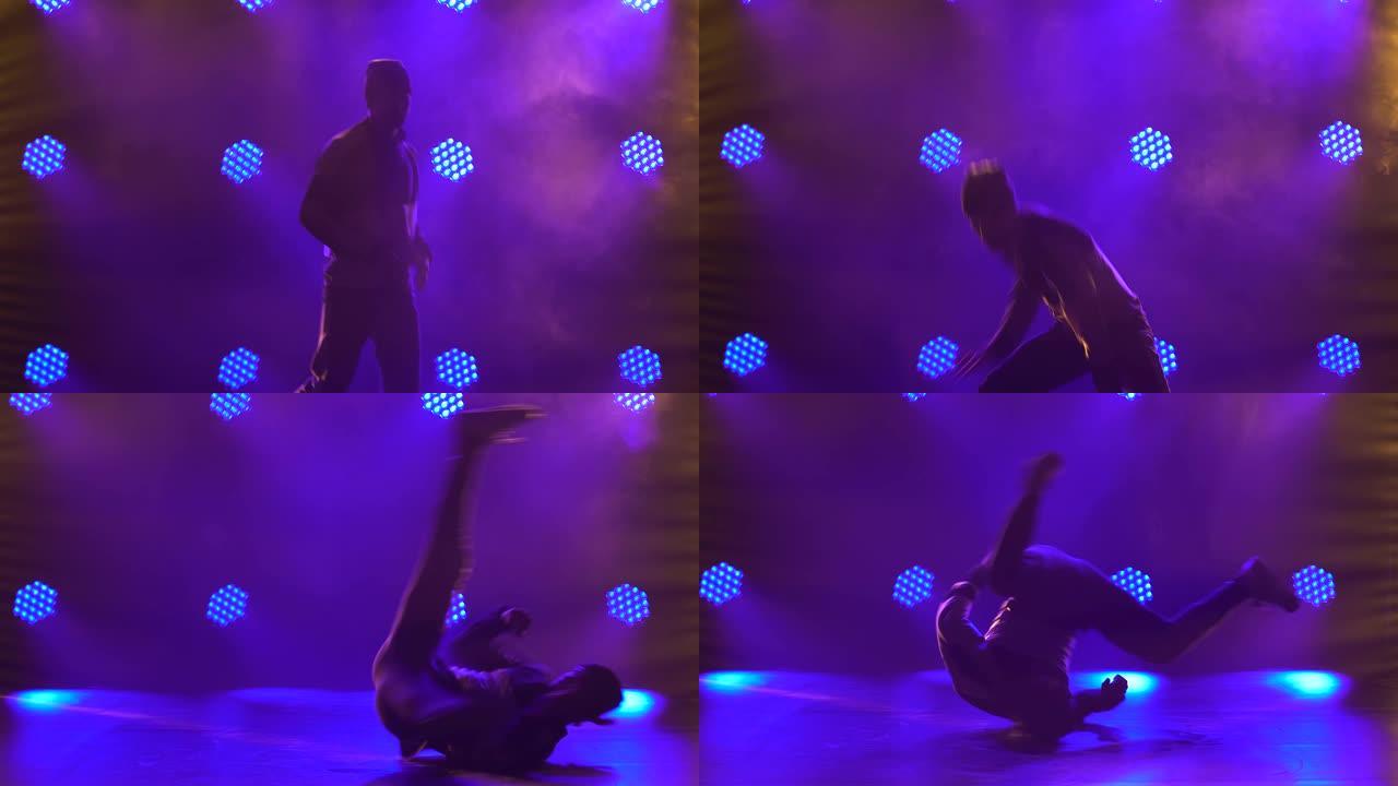 一个男舞者的剪影在工作室里跳霹雳舞、嘻哈、街舞，与世隔绝。年轻人在带有紫色背光的黑暗工作室中表演霹雳