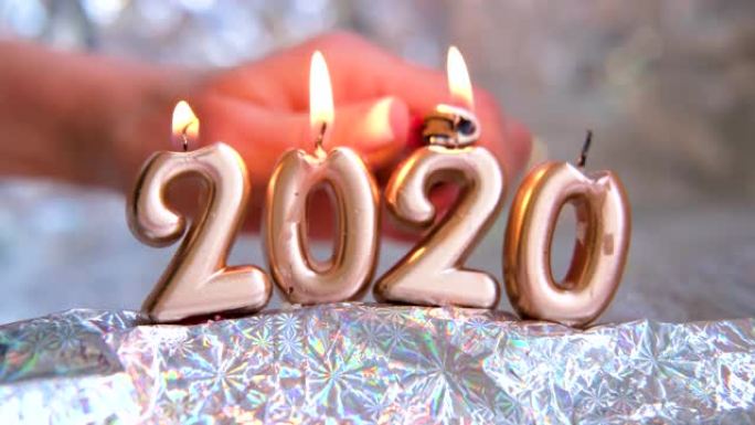 女人的手点燃烛光2020。金色蜡烛在燃烧。模糊的银色背景。圣诞快乐，新年快乐。选择性聚焦。创意现场贺