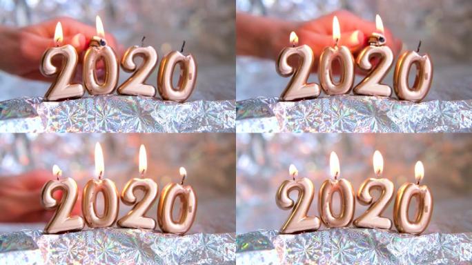 女人的手点燃烛光2020。金色蜡烛在燃烧。模糊的银色背景。圣诞快乐，新年快乐。选择性聚焦。创意现场贺