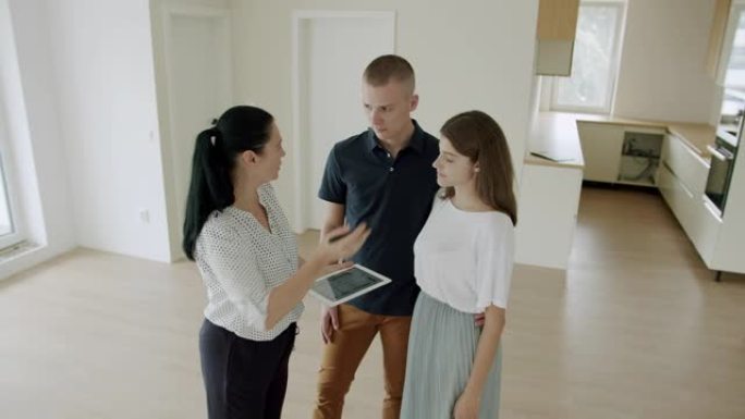 房地产经纪人用数字平板电脑向年轻夫妇展示新房子。