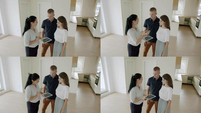 房地产经纪人用数字平板电脑向年轻夫妇展示新房子。