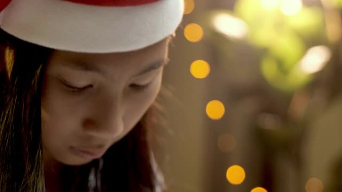 快乐的亚洲女孩戴着圣诞老人的帽子，带着圣诞灯背景微笑。