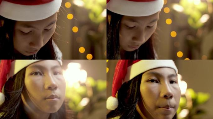 快乐的亚洲女孩戴着圣诞老人的帽子，带着圣诞灯背景微笑。