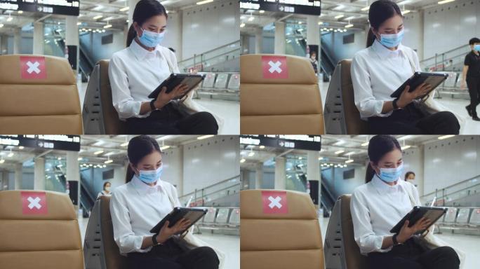 戴着外科口罩的女人面部保护，坐在机场航站楼的椅子上使用平板电脑检查社交媒体，并在新型冠状病毒肺炎大流