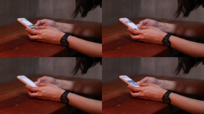 4k亚洲女性手使用白色智能手机，向下滚动手机，戴着黑色手表，手放在木桌上，在家，晚上，社交媒体，手机
