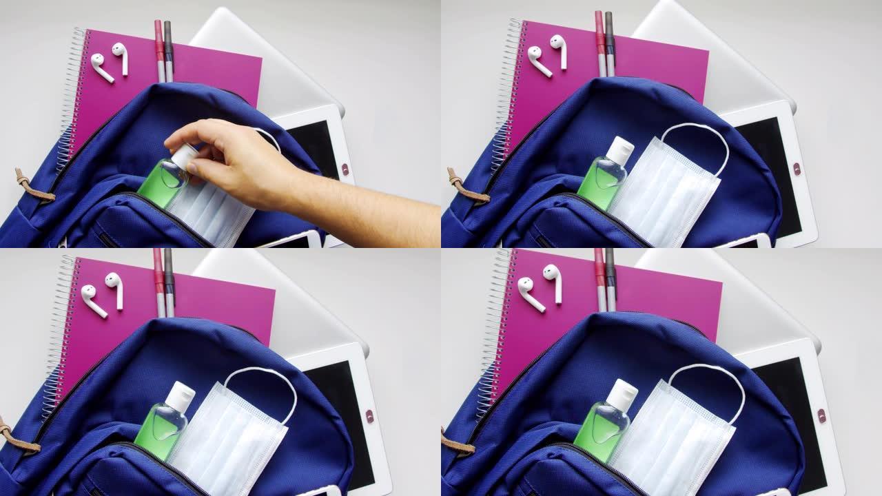 蓝色书包包，带有消毒剂和口罩，笔记本，铅笔耳机，平板电脑，计算机和智能手机。在全球大流行期间回到学校