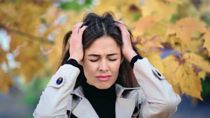 沮丧的女人哭着抱着头在秋天户外有负面情绪。4k龙红相机