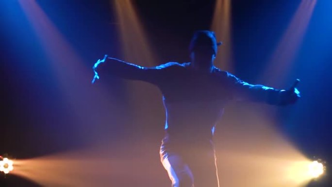 一个年轻人在聚光灯下的黑暗工作室里练习霹雳舞的剪影。特写。慢动作