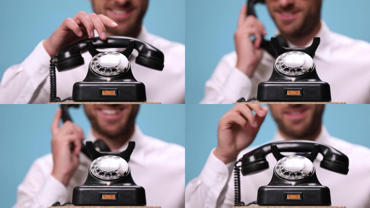 在一部旧电话上特写，一位英俊的商人说话，大笑，挂断电话，指着蓝色背景上的相机