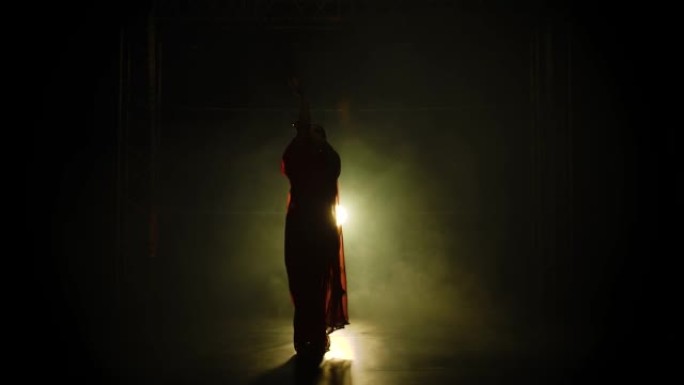 剪影一个穿着红色纱丽的年轻女孩舞者。印度民间舞蹈。在带有烟雾和霓虹灯的黑暗工作室中拍摄