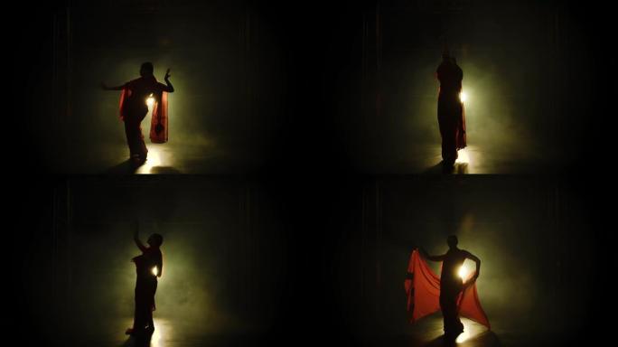 剪影一个穿着红色纱丽的年轻女孩舞者。印度民间舞蹈。在带有烟雾和霓虹灯的黑暗工作室中拍摄