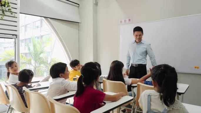 亚洲老师在学校的教室里教孩子。小男孩和女孩一起举手接受评论。教育、经验学习和技能发展的概念。