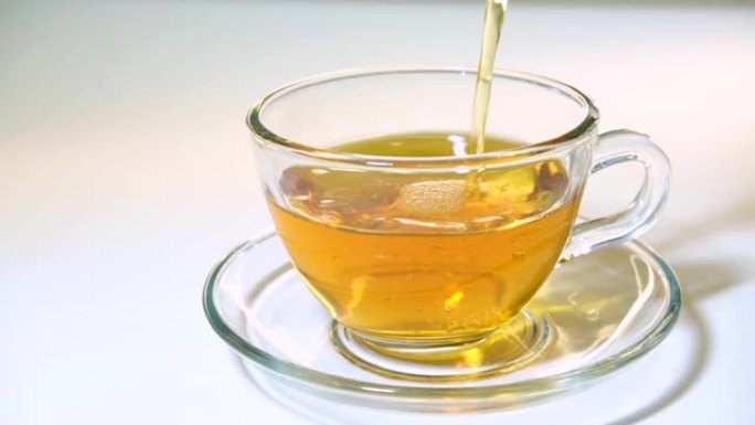 将茶壶中的芳香红茶倒入白色背景特写相配的透明玻璃茶杯中