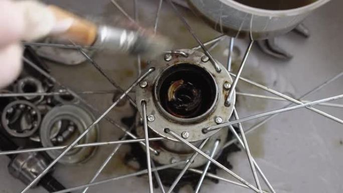戴着手套的手的特写镜头可以清洁自行车车轮的后轮毂。用清洗液和刷子清洗自行车零件。