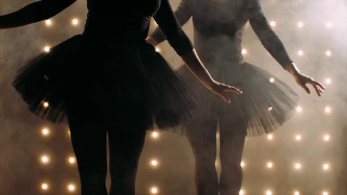 两个穿着黑色短裙的芭蕾舞演员的剪影正在黑暗的工作室里跳芭蕾舞。