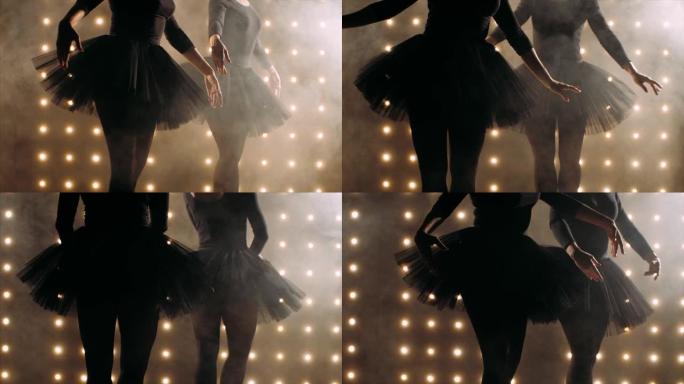 两个穿着黑色短裙的芭蕾舞演员的剪影正在黑暗的工作室里跳芭蕾舞。