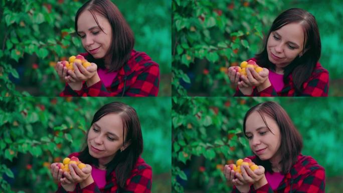 年轻漂亮的女人手里拿着杏子。成年雌性，成熟果实在杏树的背景上微笑