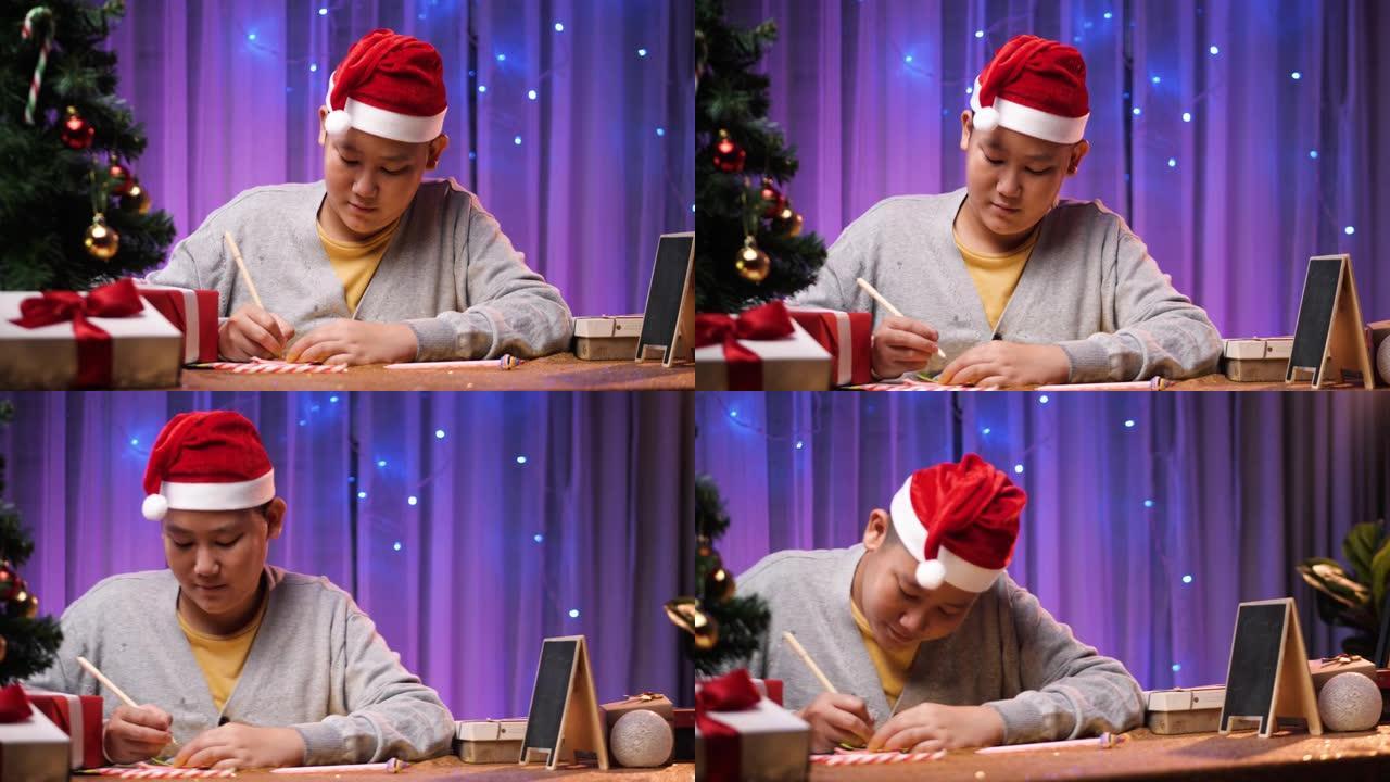 快乐的亚洲男孩戴着圣诞老人的帽子，在家用圣诞灯背景在礼品盒上写信息。