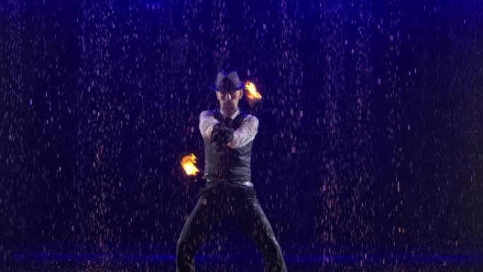 时尚男人表演的迷人的雨和水滴中的火表演。带有蓝色背光的烟熏工作室背景。慢动作。特写