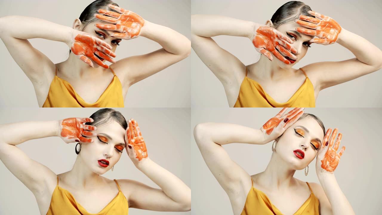 人体艺术。女人用橙色油漆的手掌遮住脸。