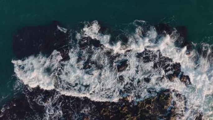 汹涌的海水的无人驾驶空中俯视图的前方。绿松石海水的风景鸟瞰图，沿海石头上有强烈的波浪产生的白色泡沫。