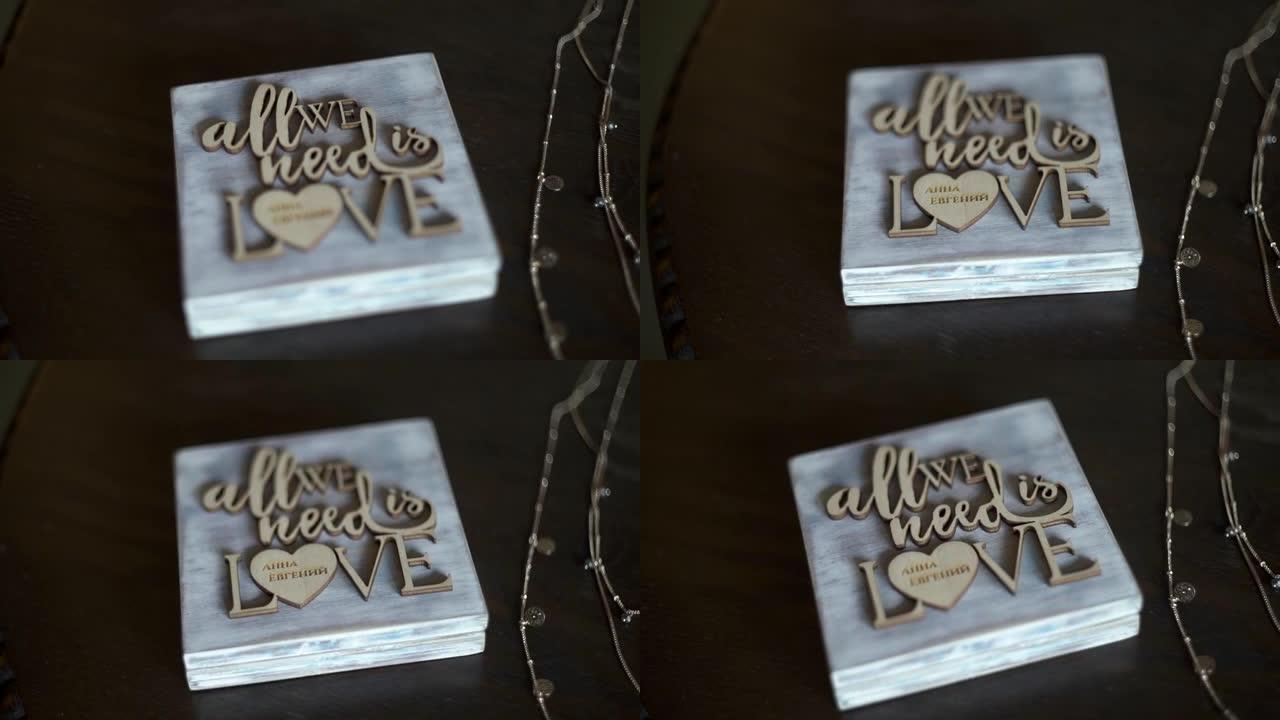 结婚戒指的木盒，上面有名字和文字: “我们所需要的只是爱”。珠宝，配饰，吊坠，金链，特写，慢动作。专