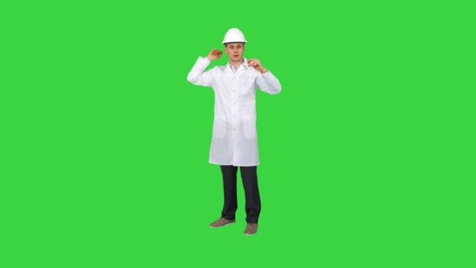 在绿色屏幕上工作后，戴着头盔跳舞的年轻工程师，色键