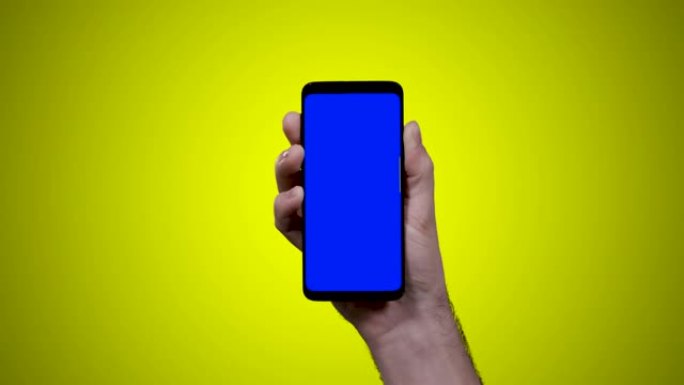 男子手持智能手机，黄色背景上的蓝色croma键向左侧滑动一次