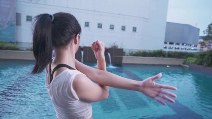 年轻的亚洲女性伸展手臂和肩膀看游泳池城市高层居民公寓设施，灵活的上半身，美丽放松，锻炼动力，后视