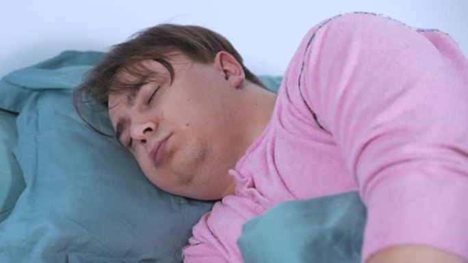 穿着粉红色睡衣的疲倦的年轻人睡在床上温暖的毯子下，大声打鼾，嘴唇发抖。有呼吸问题的病人在家休息