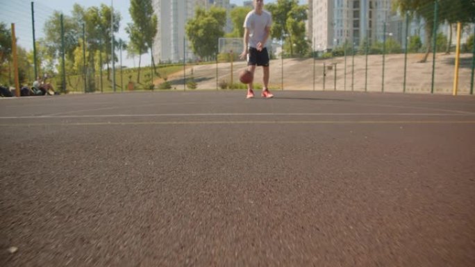 特写肖像年轻活跃的高加索男子篮球运动员在球场上的篮筐里扔球，背景是城市建筑