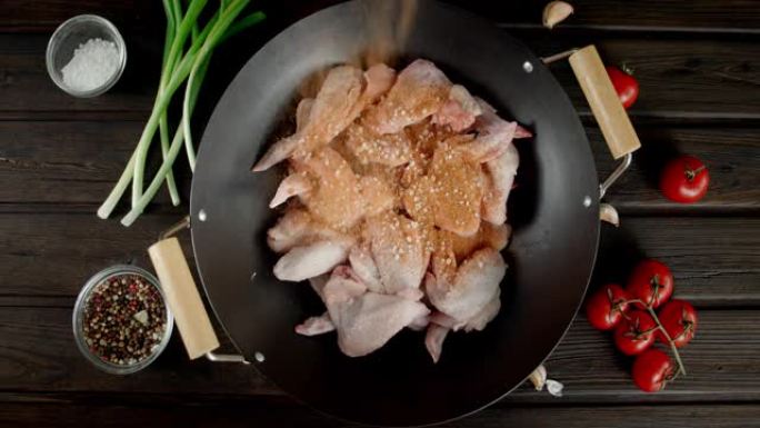 在煎锅里的生鸡翅上撒上香料。