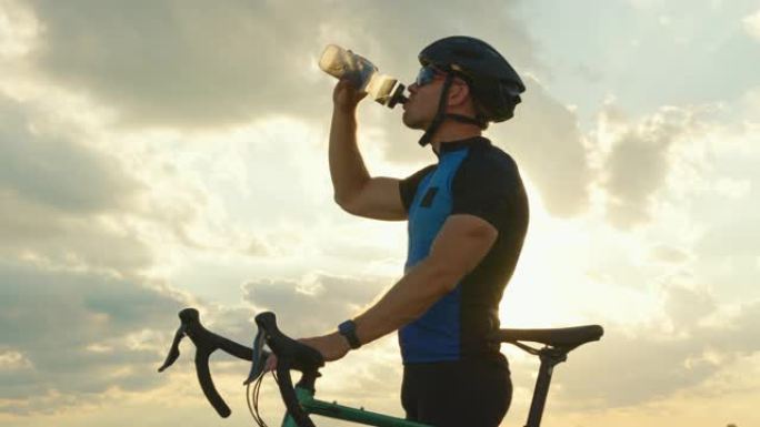 骑自行车的人站在路边，从背景日落的瓶子里喝水。特写拍摄。4K