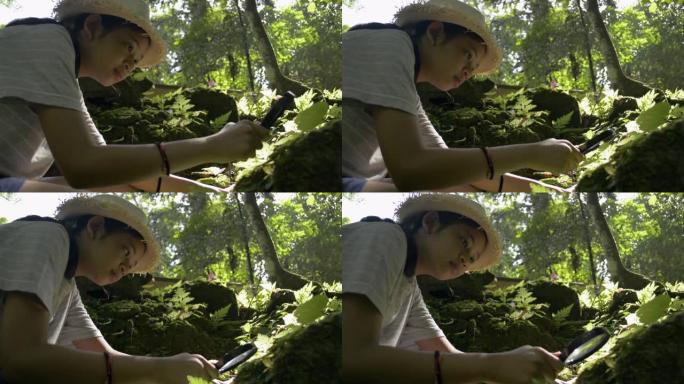 戴着草帽的亚洲可爱女孩用放大镜看看热带雨林中绿色植物区系的细节。