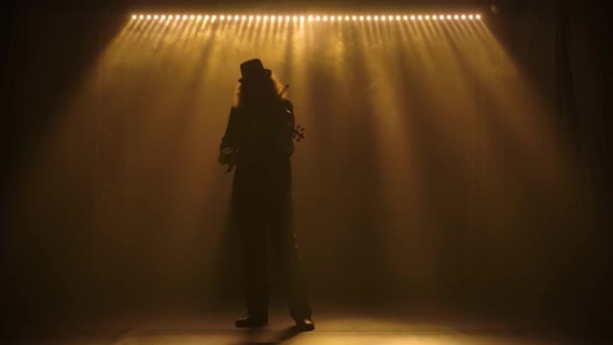 一位剪影的小提琴手音乐家，头发茂密，戴着帽子，演奏古典木制小提琴。在黑暗的烟熏工作室中拍摄，灯光慢动