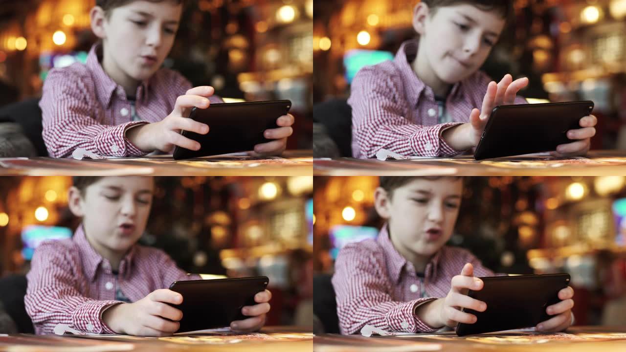 快乐男孩在智能手机上玩赛车游戏正坐在餐厅的椅子上，背景明亮的室内灯光。一家人正在等待午餐