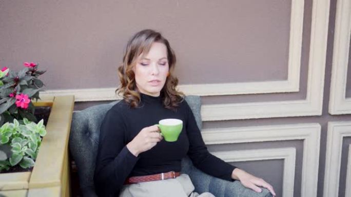 一个女孩坐在桌子旁，端着一杯茶或咖啡，聊天。