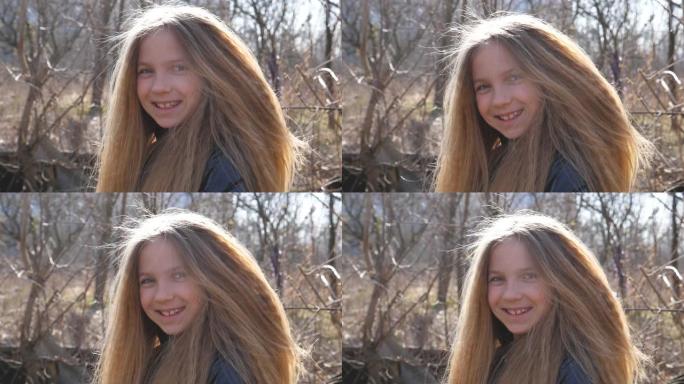 快乐的金发女孩看着镜头，在户外大笑。早春森林模糊背景下女性微笑的孩子的肖像。小孩子脸上的积极情绪。