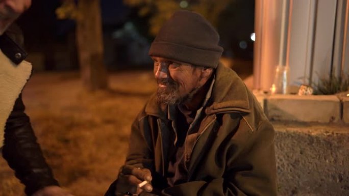 路人晚上在人行道上和无家可归的人说话。