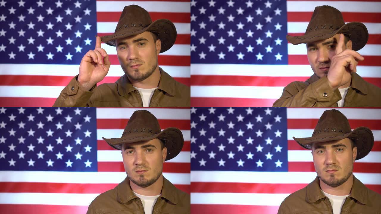 在美国国旗的背景下，一个戴着牛仔帽和皮夹克的男人用他的手指沿着帽子的边缘