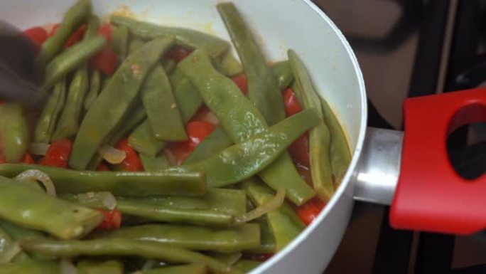 美味的青豆在平底锅上煎炸，配以新鲜的西红柿。女人用木勺翻营养盘。健康素食