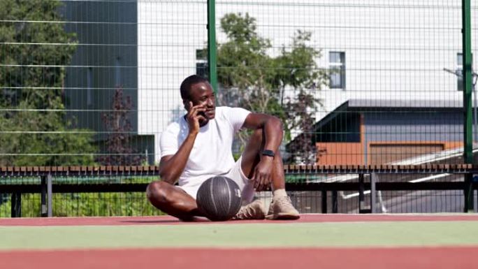 中断训练。年轻的非洲裔美国人在篮球场上用手机聊天